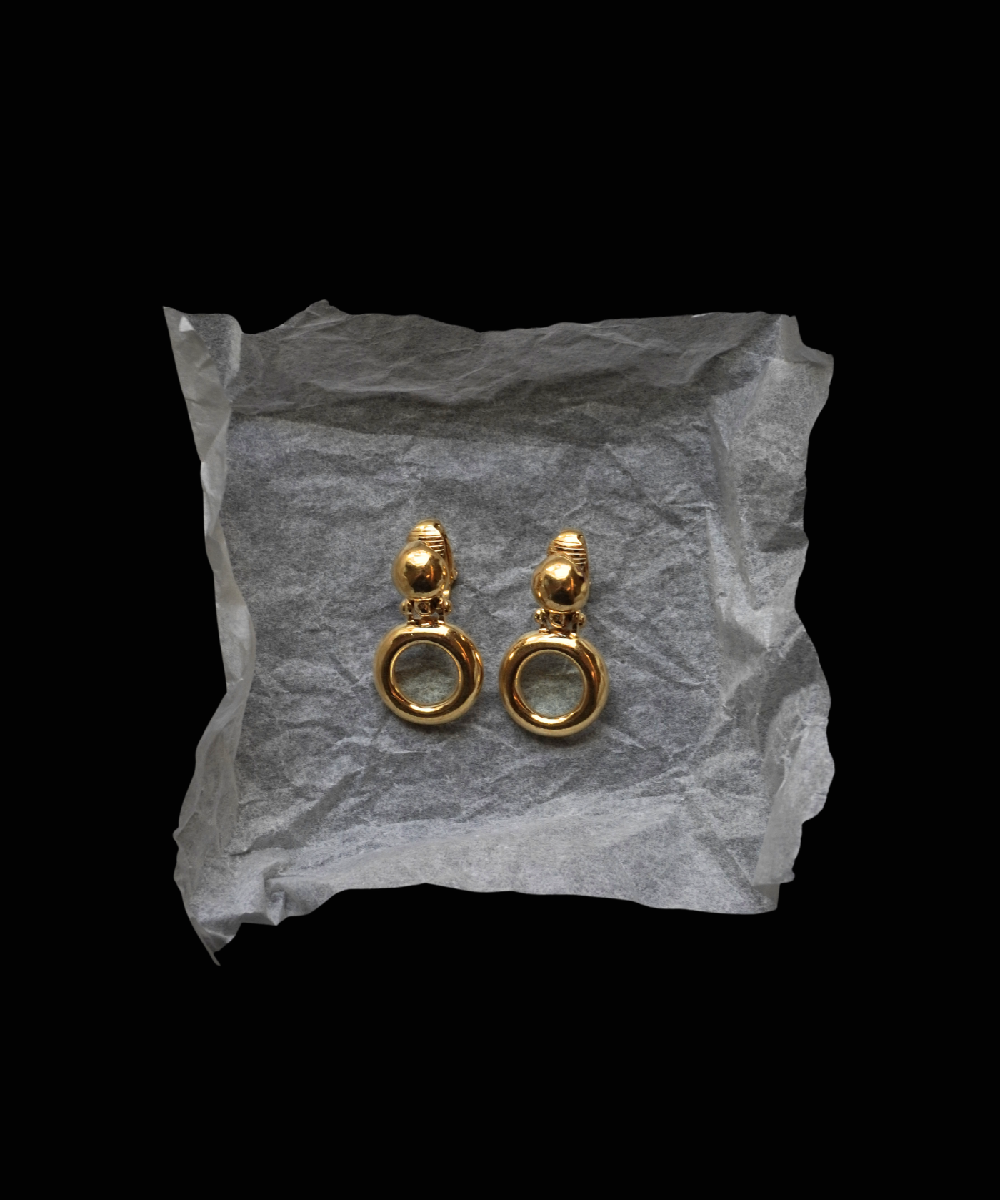 Gold earrings on crumpled gray paper against a black background
