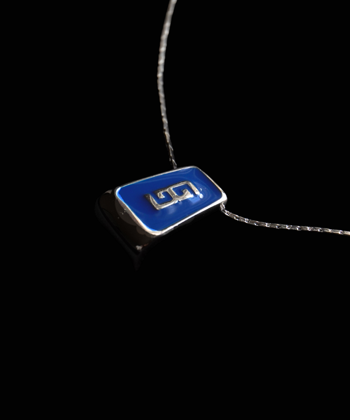 A Givenchy silver-toned necklace with a rectangular pendant featuring a vibrant blue enamel background and a stylized gold monogram logo, set against a solid black background.