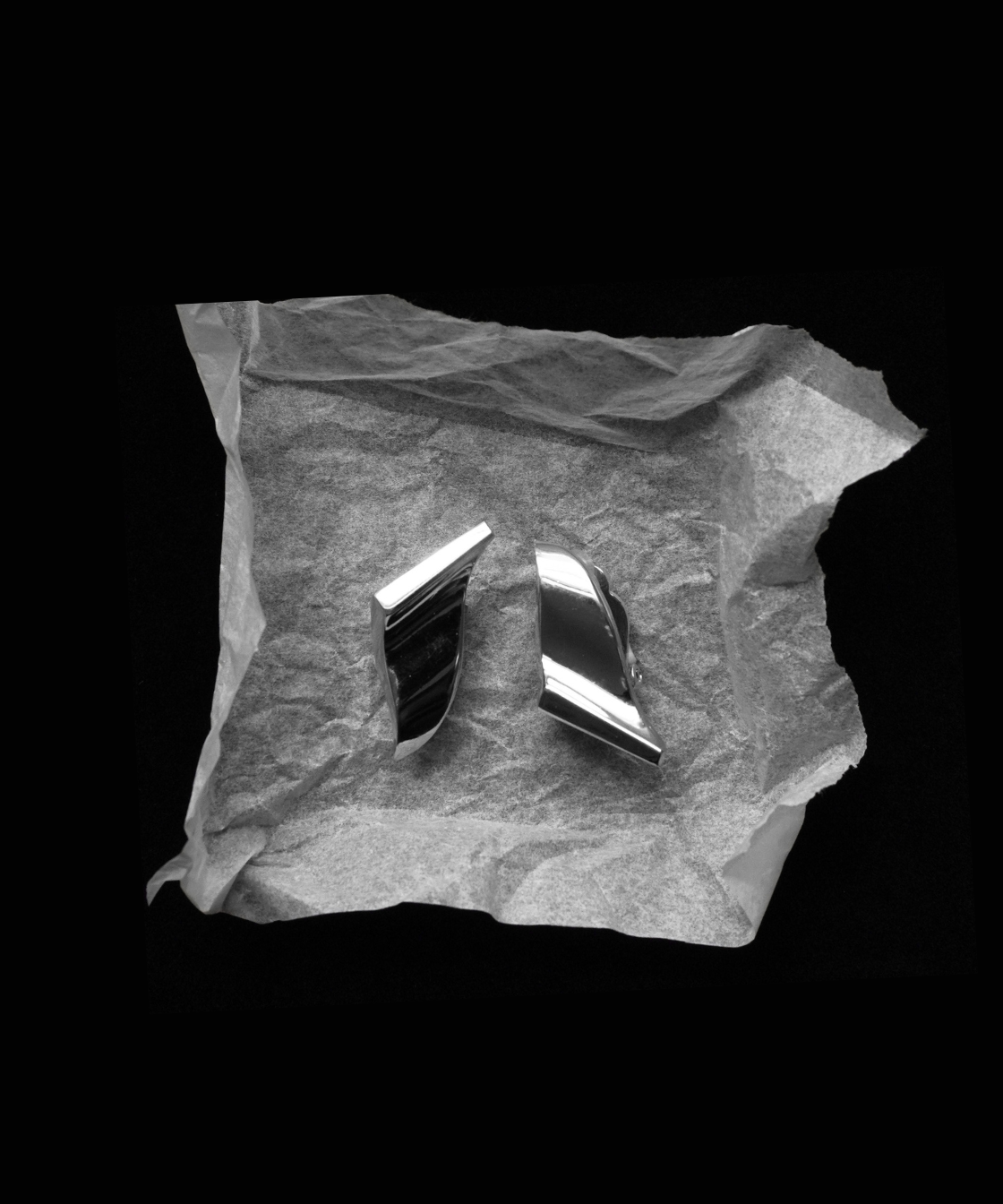 Two polished metallic Givenchy Silver Earrings, on crumpled gray paper against a solid black background.