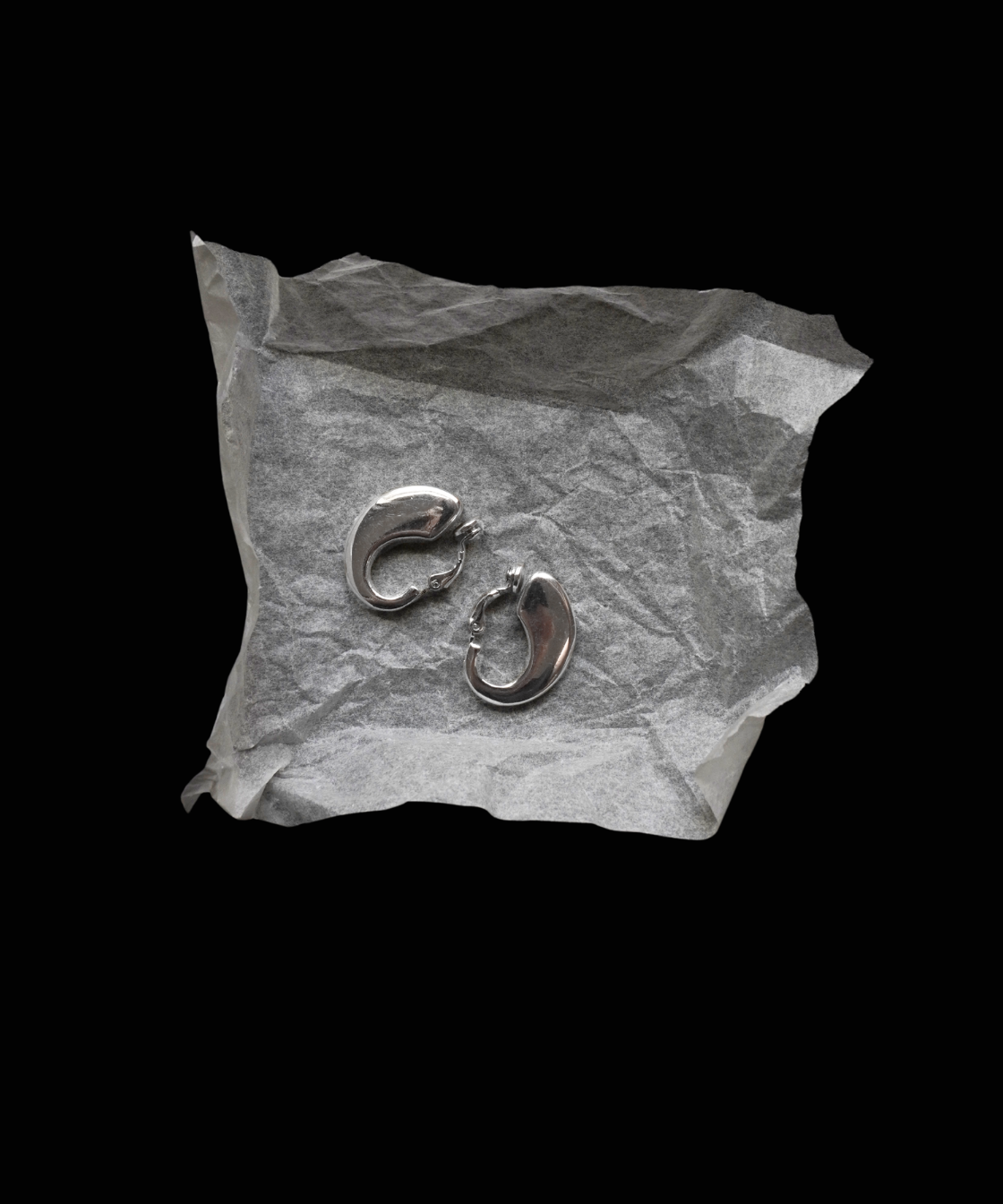 Pair of silver earrings on crumpled paper against a black background