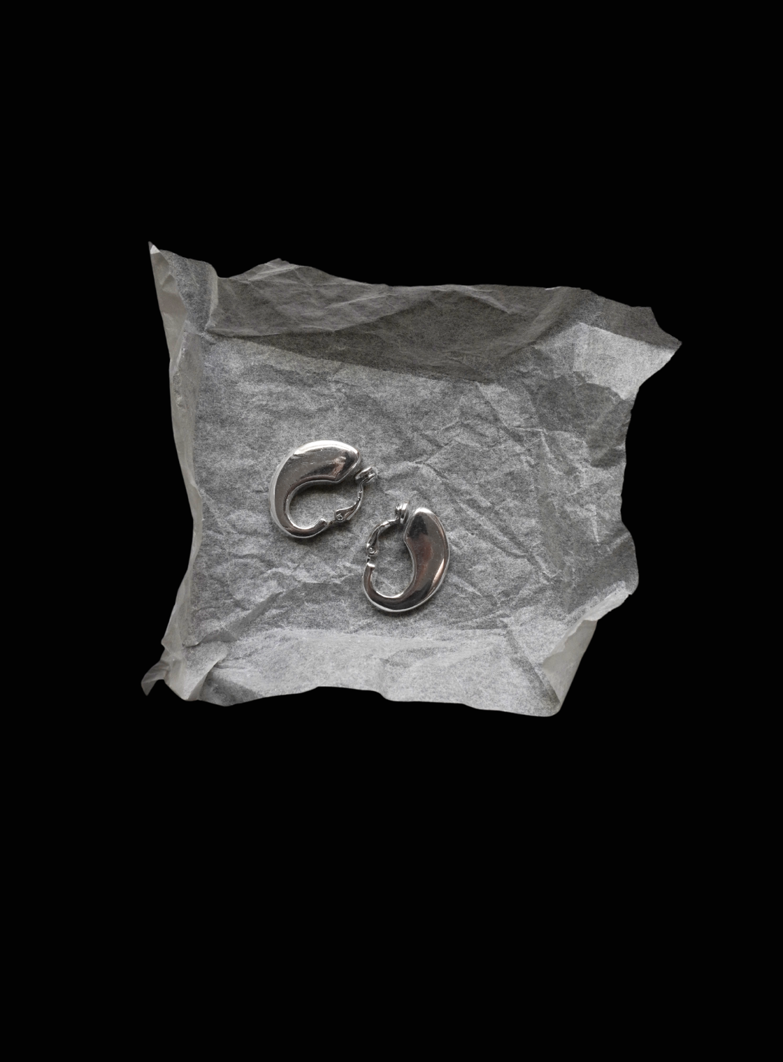 Pair of silver earrings on crumpled paper against a black background