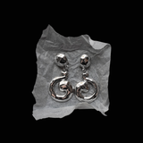A pair of silver-toned dangle earrings with a textured spiral drop design, displayed on a crumpled piece of white paper against a solid black background.