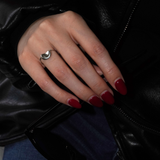 A close-up of a hand wearing a silver ring with a crescent moon design, resting on a black leather jacket. The nails are painted dark red, and blue jeans are visible underneath.