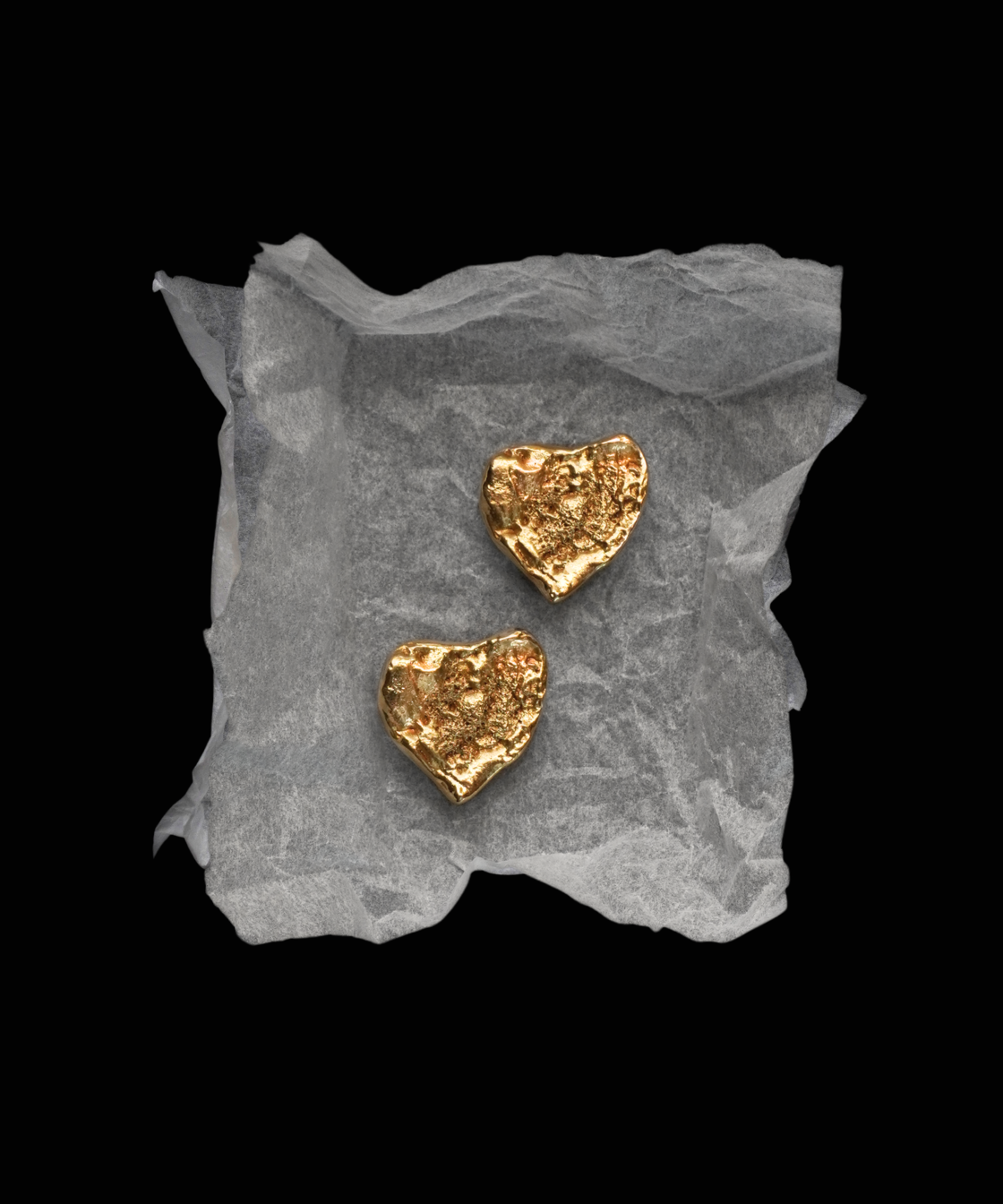 Gold heart-shaped earrings YSL Gold Earrings on a textured gray surface with a black background