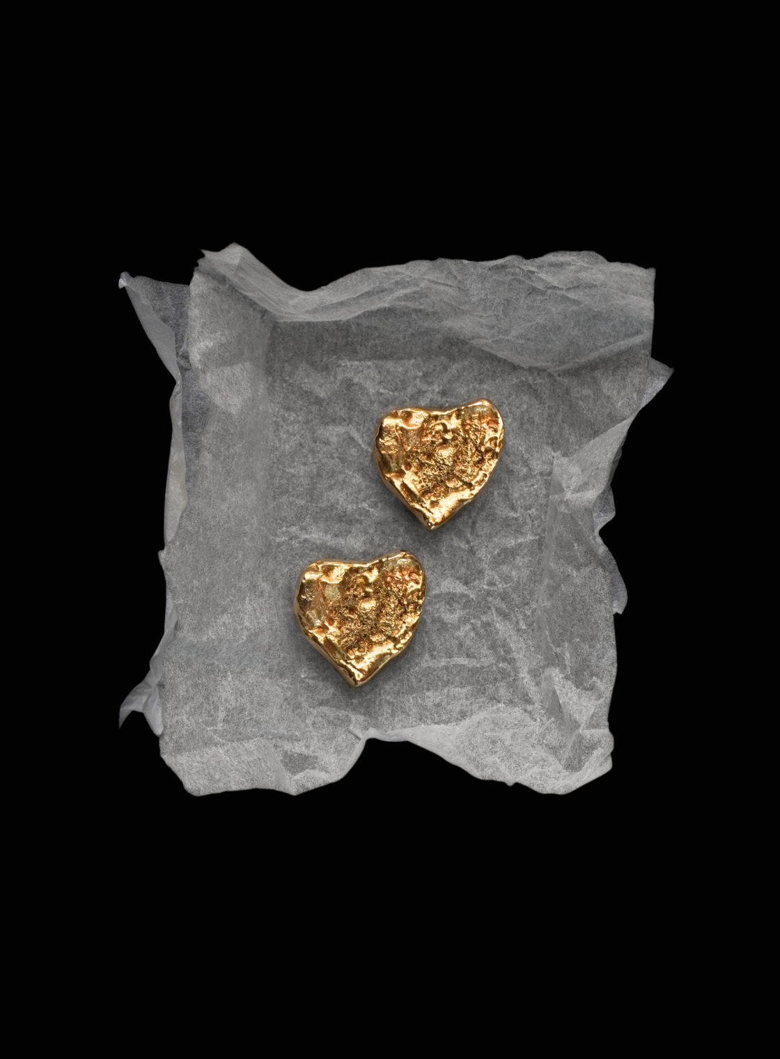 Gold heart-shaped earrings YSL Gold Earrings on a textured gray surface with a black background