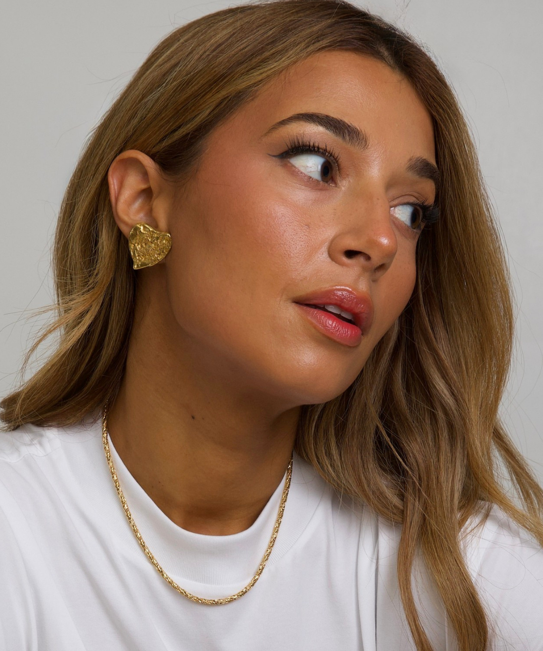 Woman wearing gold YSL earrings and a necklace against a plain background