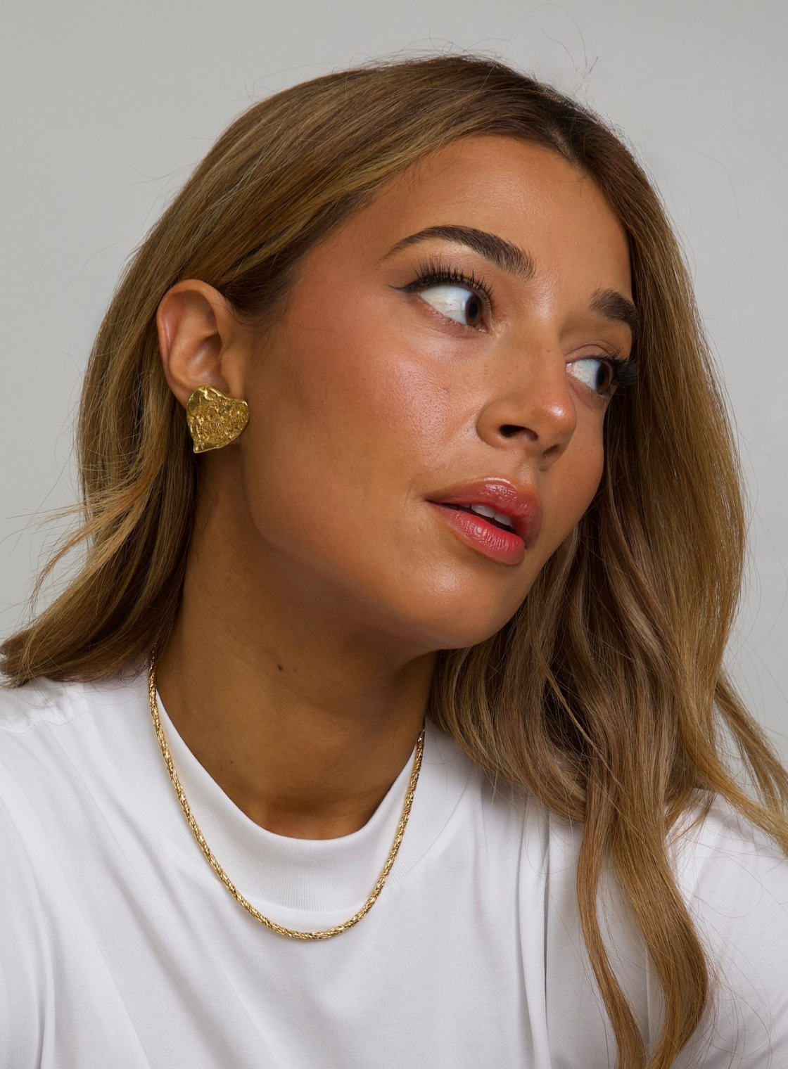 Woman wearing gold YSL earrings and a necklace against a plain background