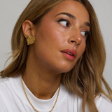 Woman wearing gold YSL earrings and a necklace against a plain background