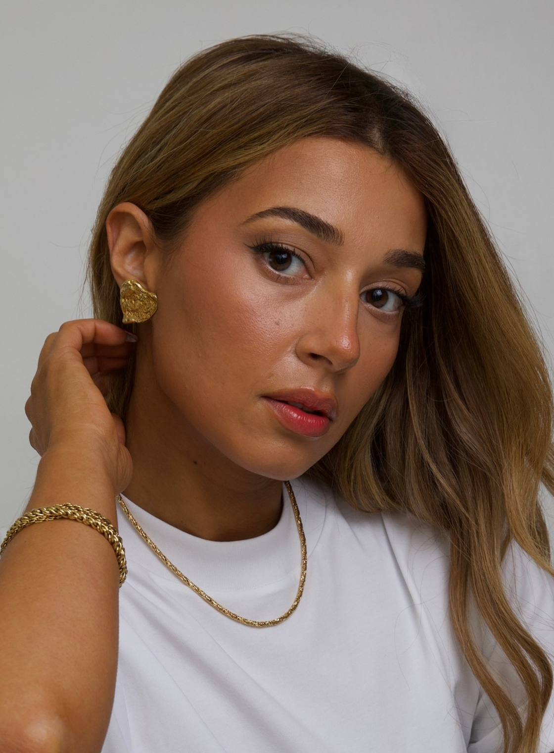 Woman wearing gold YSL Gold earrings and a necklace against a plain background
