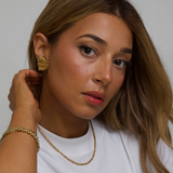 Woman wearing gold YSL Gold earrings and a necklace against a plain background