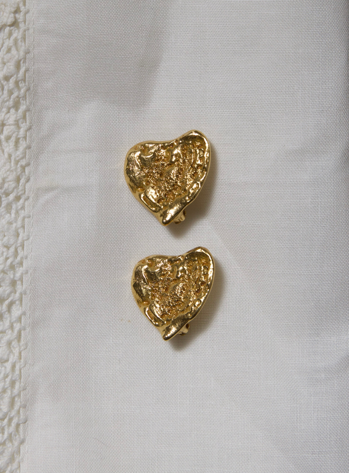 Gold YSL heart-shaped earrings on a white fabric background