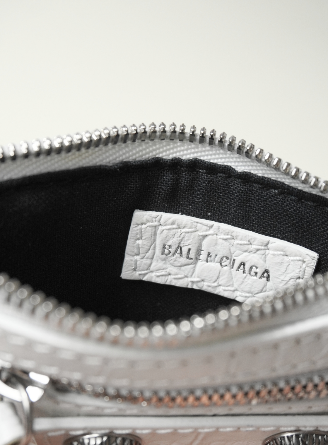 Close-up of the interior of a silver Balenciaga handbag, showing a black fabric lining and a white textured paper brand label sewn onto the inside of the zipper.