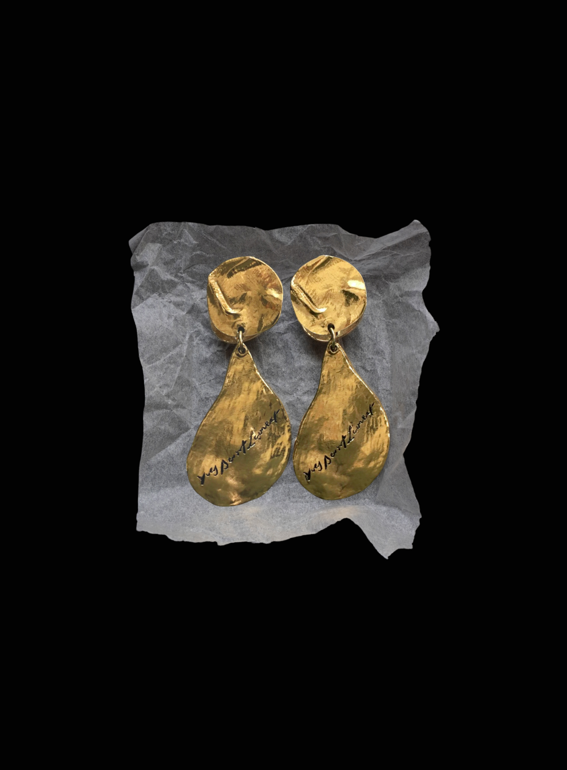 Pair of gold YSL earrings on a black background.